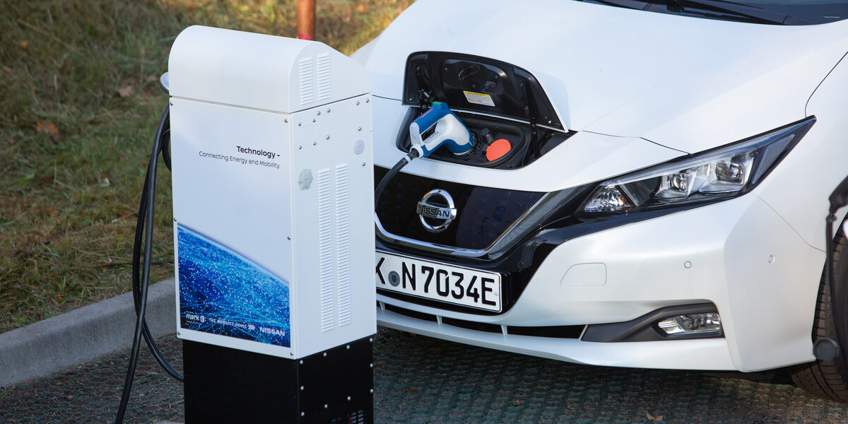 Une voiture électrique Nissan Leaf branchée à une borne de recharge électrique moderne, illustrant la connexion entre l'énergie et la mobilité durable.