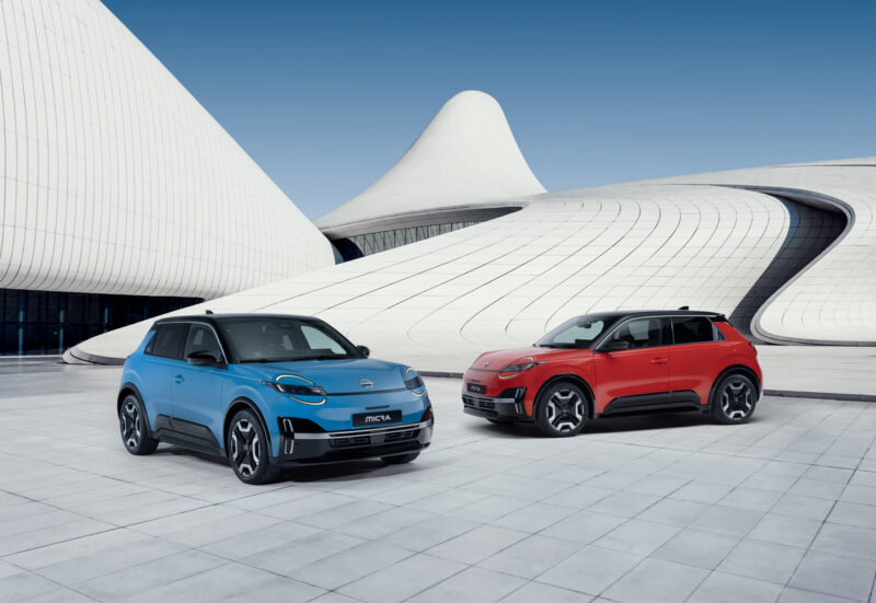 Deux Nissan Micra, l’une bleue (Gear Blue) et l’autre rouge, stationnées en V face à face devant un bâtiment architectural au design bleu et blanc